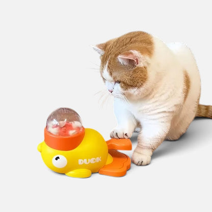 Tailora cat playing with a yellow and orange duck-shaped interactive treat dispenser toy on a light background