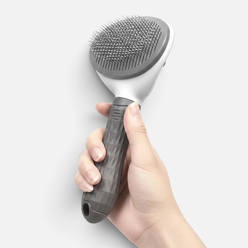 Tailora self-cleaning slicker brush with stainless steel bristles and a grey ergonomic non-slip handle held in hand